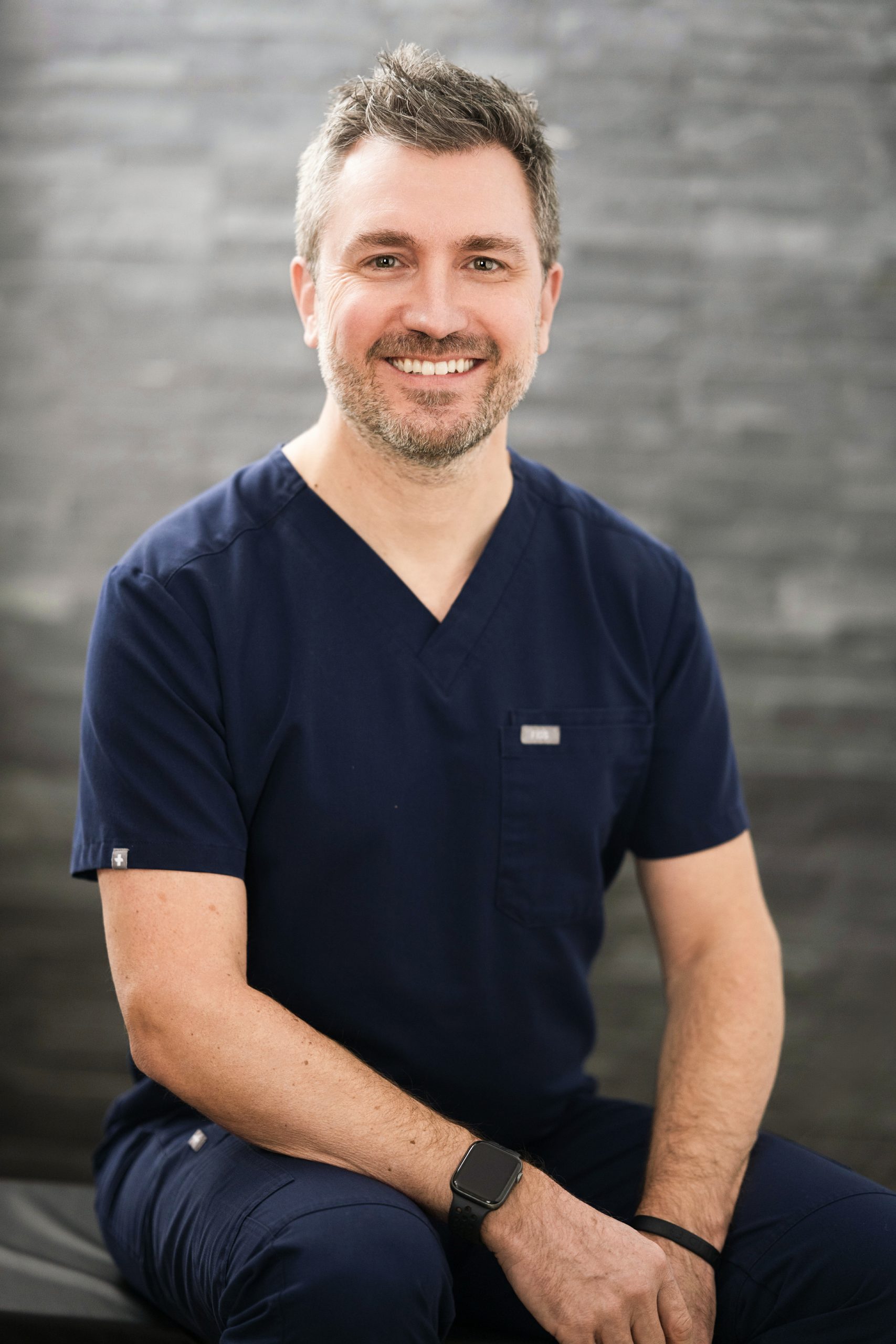 Portrait d’un professionnel dentaire en uniforme bleu marine, assis et souriant.