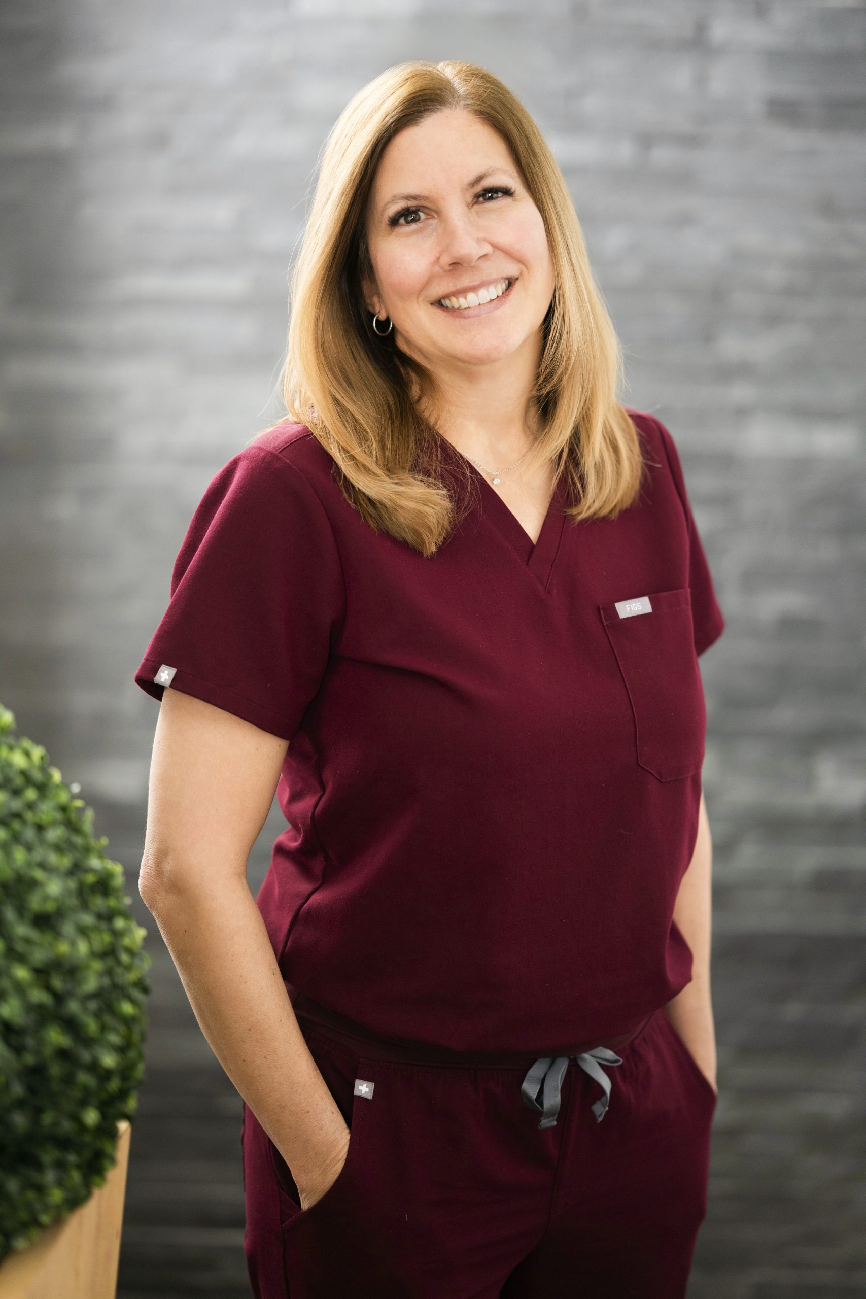 Portrait d’une professionnelle dentaire en uniforme bordeaux, souriante.